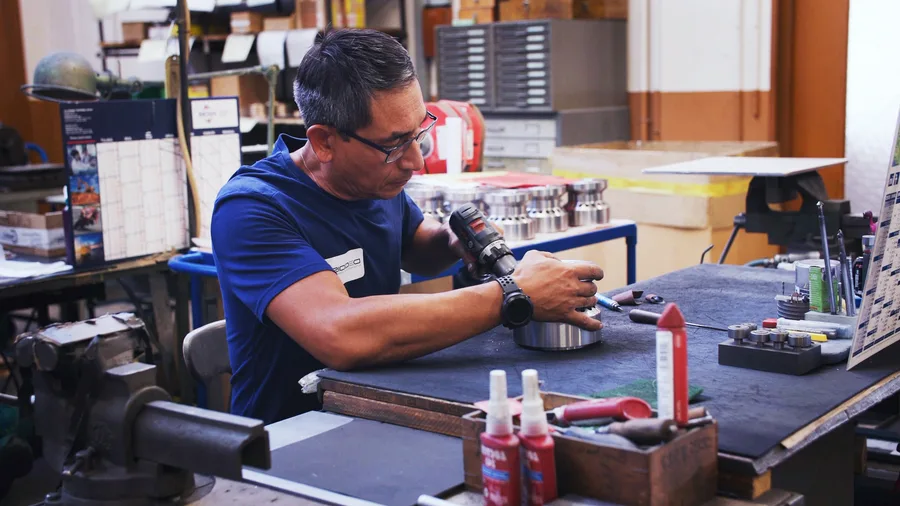 Dans un atelier, un technicien assemble une pièce métallique à la visseuse, entouré de ses outils.