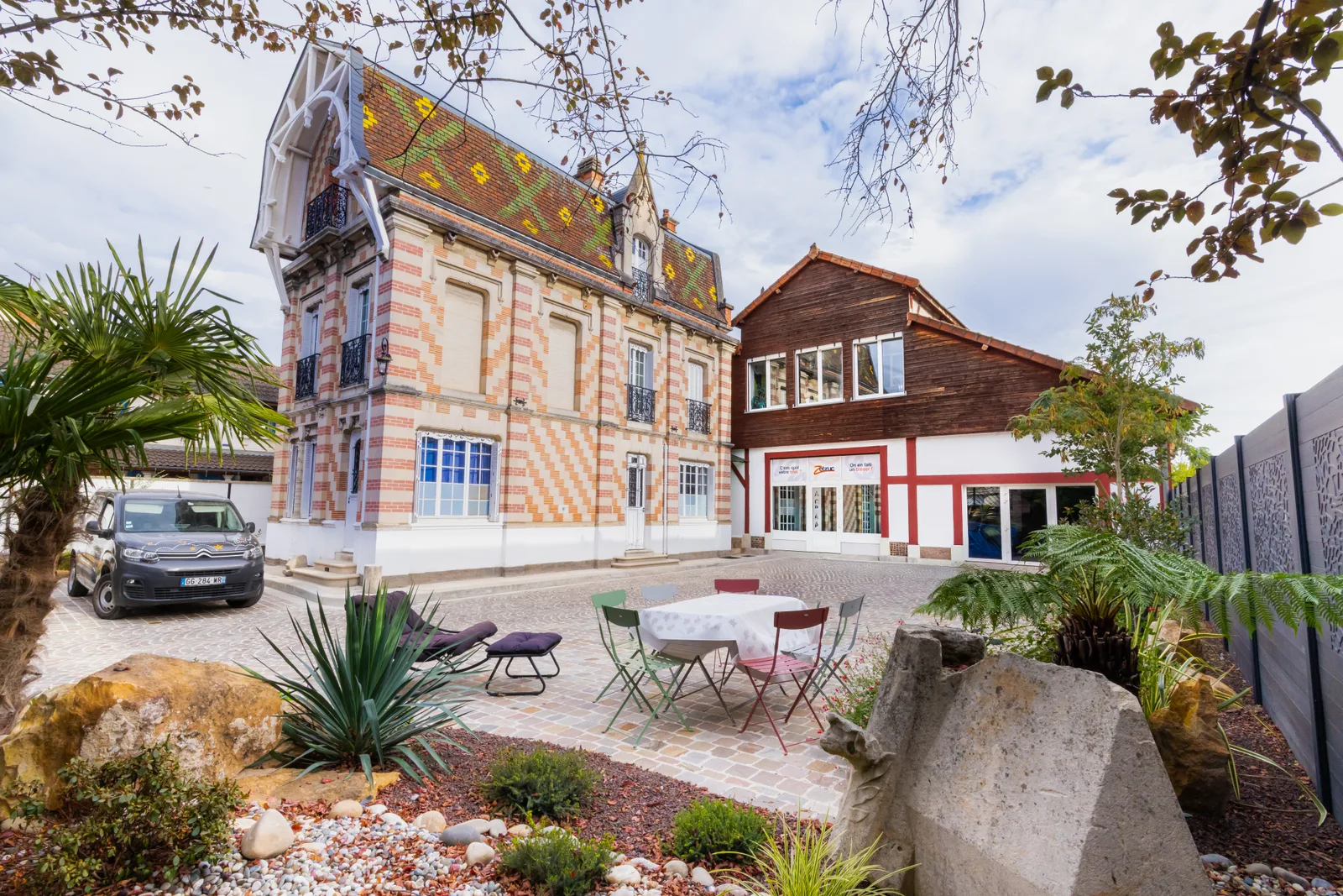 La cour pavée de l'agence Zetruc à Troyes, devant la maison en briques et le bâtiment rouge et blanc de l'agence